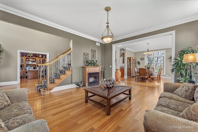 living room with crown molding, a notable chandelier, light wood finished floors, stairs, and baseboards