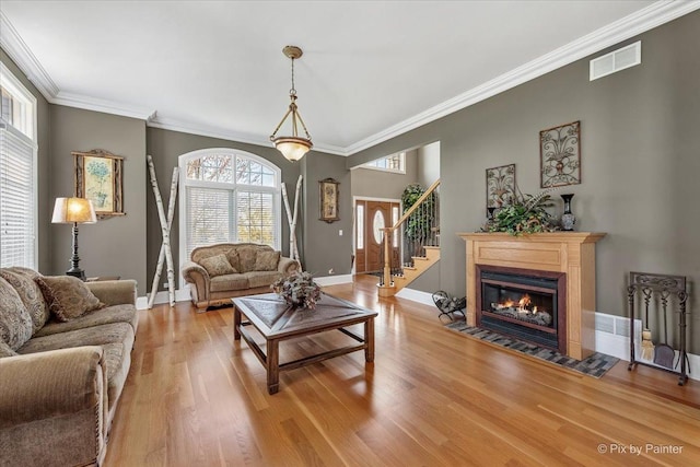 living area featuring visible vents, light wood-style floors, crown molding, and baseboards