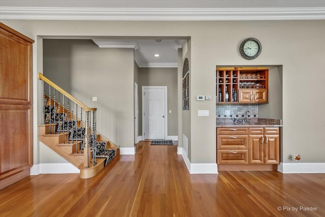 interior space with indoor wet bar, crown molding, wood finished floors, and stairway