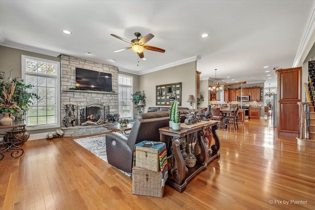 living room with a stone fireplace, crown molding, plenty of natural light, and ceiling fan with notable chandelier