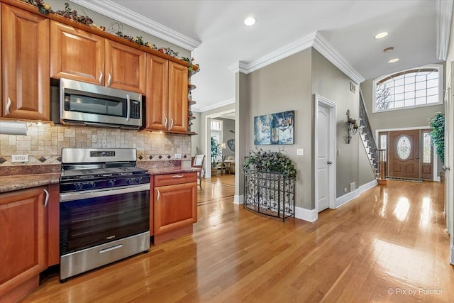 kitchen featuring decorative backsplash, brown cabinetry, appliances with stainless steel finishes, ornamental molding, and light wood-style flooring