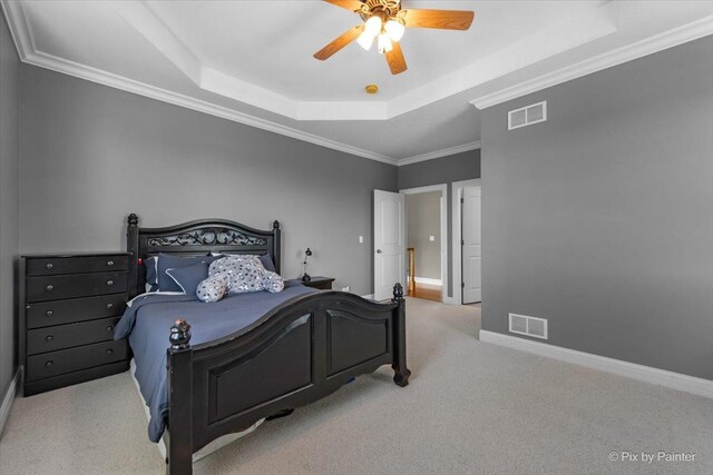 carpeted bedroom featuring visible vents, baseboards, crown molding, and a tray ceiling