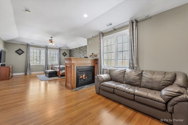 living area featuring light wood-style floors, ceiling fan, a fireplace with flush hearth, and visible vents
