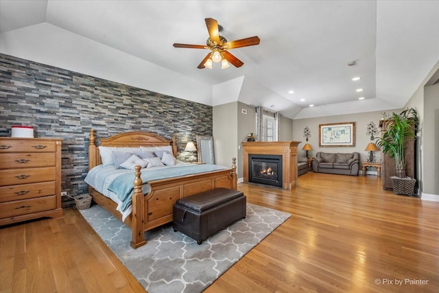 bedroom with a ceiling fan, vaulted ceiling, wood finished floors, a glass covered fireplace, and recessed lighting