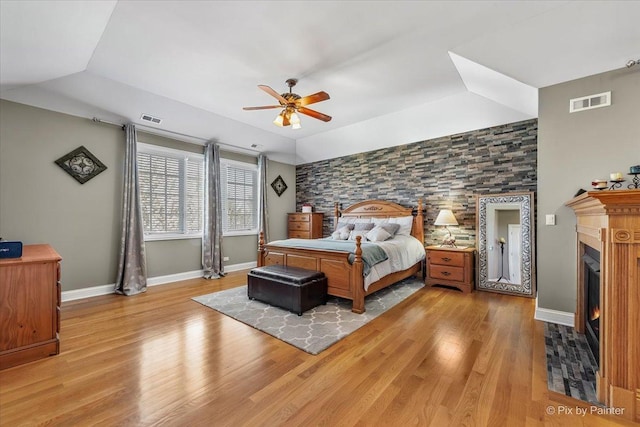 bedroom with light wood-style floors, a warm lit fireplace, and visible vents