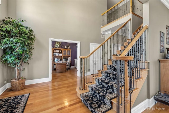staircase with baseboards, a high ceiling, and wood finished floors