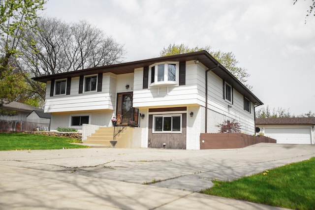 split foyer home with a detached garage, brick siding, and fence