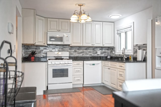 kitchen featuring white appliances, dark countertops, a sink, and tasteful backsplash