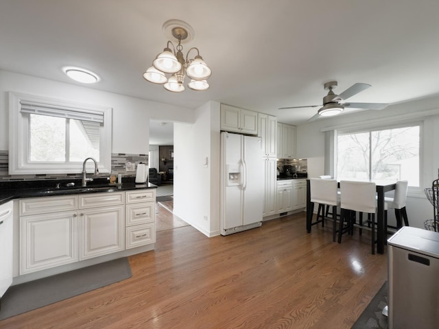kitchen with a sink, white fridge with ice dispenser, ceiling fan with notable chandelier, and tasteful backsplash