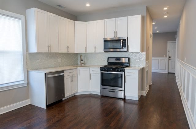 2957 N Avers Ave, Chicago, IL 60618 - kitchen with stainless steel appliances, light countertops, decorative backsplash, a sink, and white cabinets