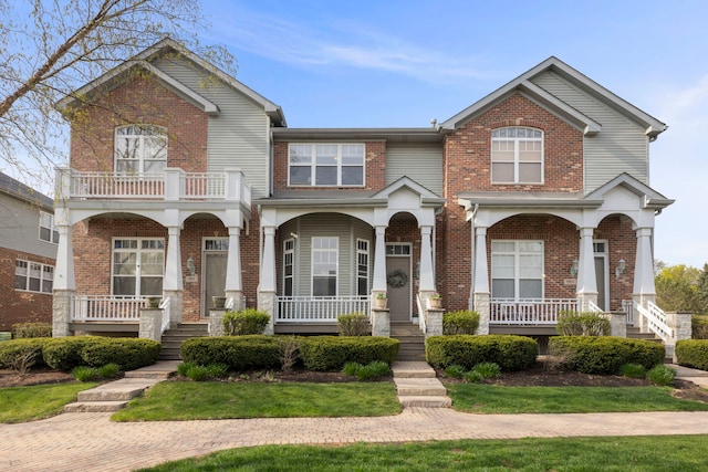 view of front of home featuring brick siding, a balcony, and covered porch