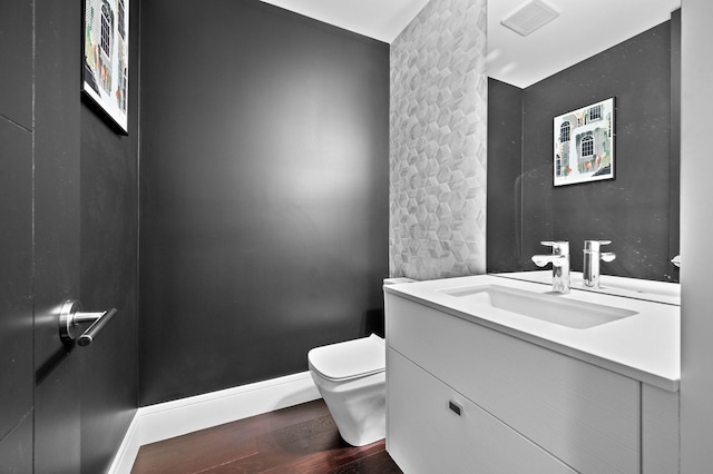 half bath featuring toilet, visible vents, wood finished floors, and vanity