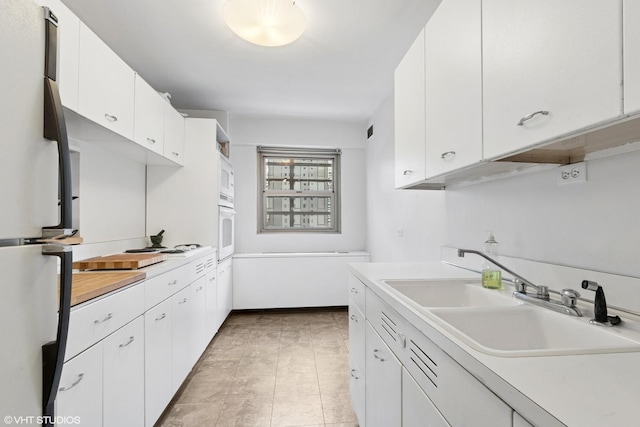 kitchen featuring a sink, light countertops, white appliances, and white cabinetry