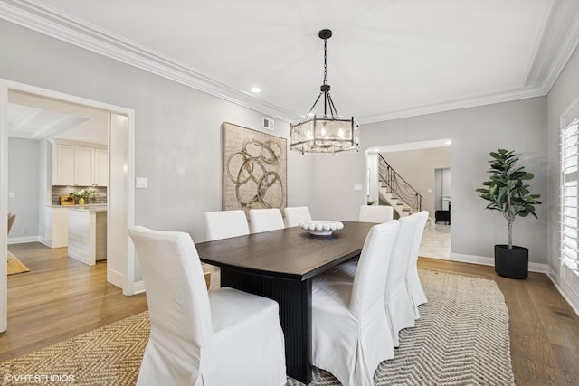 dining area with a chandelier, light wood-style flooring, stairs, visible vents, and ornamental molding