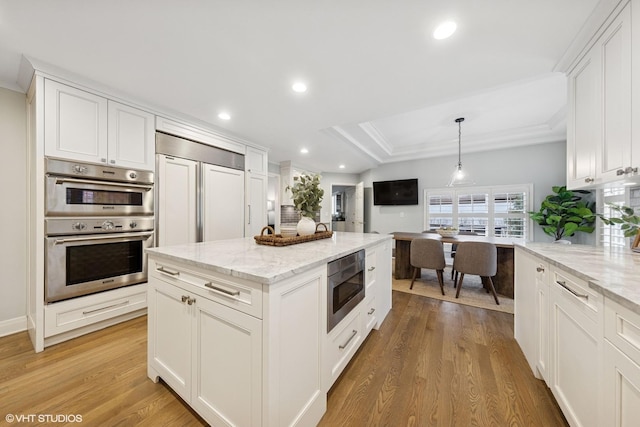 kitchen featuring light wood-style floors, ornamental molding, white cabinetry, and built in appliances