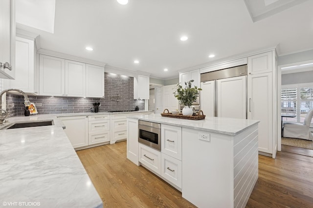 kitchen featuring light stone counters, a sink, built in appliances, and light wood-type flooring
