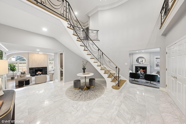 foyer with recessed lighting, marble finish floor, a warm lit fireplace, and stairway