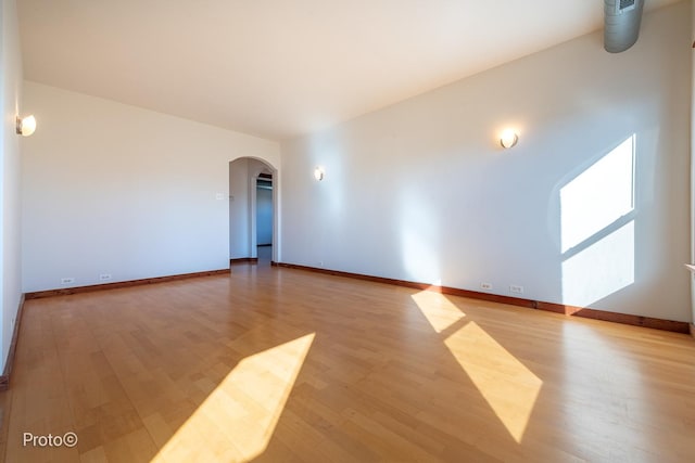 unfurnished room with arched walkways, baseboards, and wood finished floors