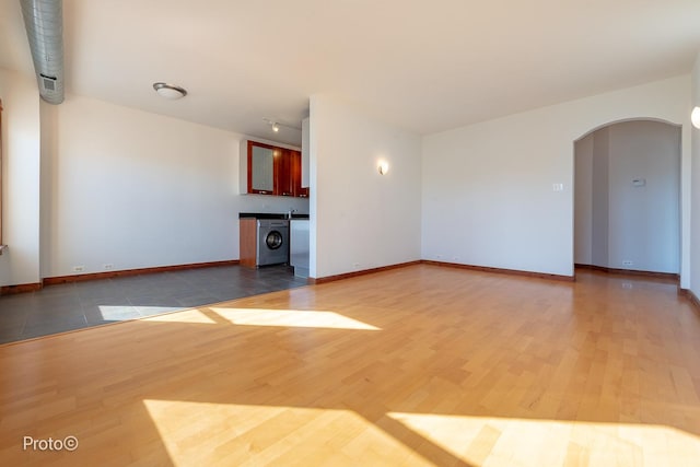 unfurnished living room with baseboards, arched walkways, washer / dryer, and wood finished floors