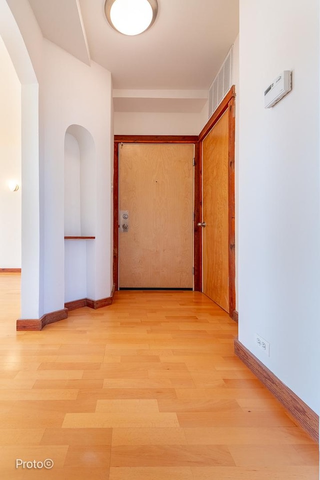 hallway with baseboards, visible vents, and light wood finished floors