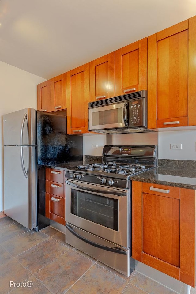 kitchen with brown cabinetry, dark stone countertops, and stainless steel gas range oven