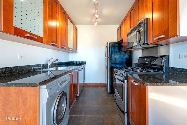 kitchen with brown cabinets, appliances with stainless steel finishes, a sink, washer / clothes dryer, and dark stone counters