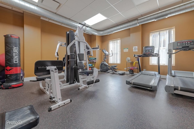 gym with baseboards, plenty of natural light, and a drop ceiling