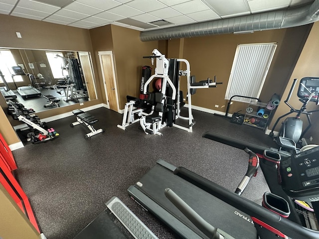 exercise room with baseboards and a drop ceiling