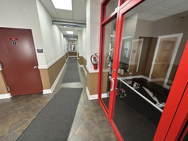 hall featuring baseboards, a paneled ceiling, and tile patterned flooring