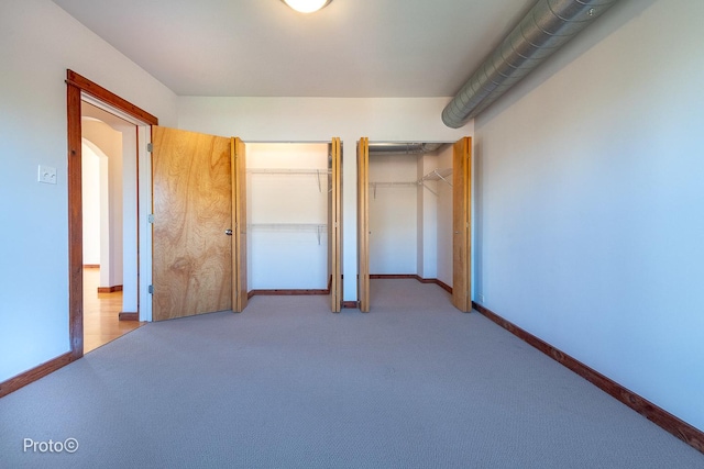 unfurnished bedroom featuring multiple closets, baseboards, carpet flooring, and arched walkways