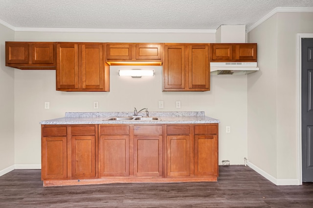 kitchen with brown cabinetry, a sink, baseboards, dark wood-style floors, and under cabinet range hood