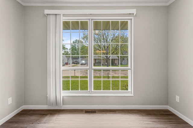 empty room with crown molding, baseboards, visible vents, and wood finished floors