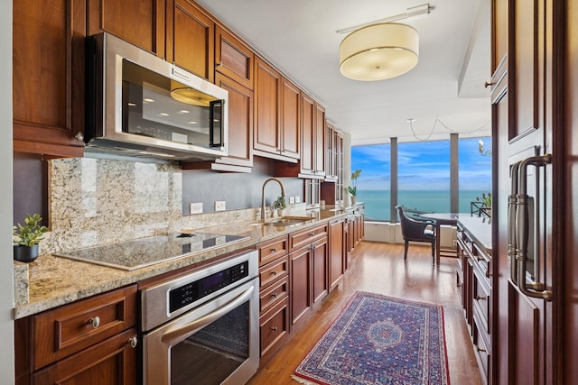 kitchen with appliances with stainless steel finishes, tasteful backsplash, light stone countertops, a sink, and dark wood-style floors