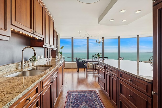 kitchen with wood finished floors, a sink, light stone counters, a chandelier, and a water view