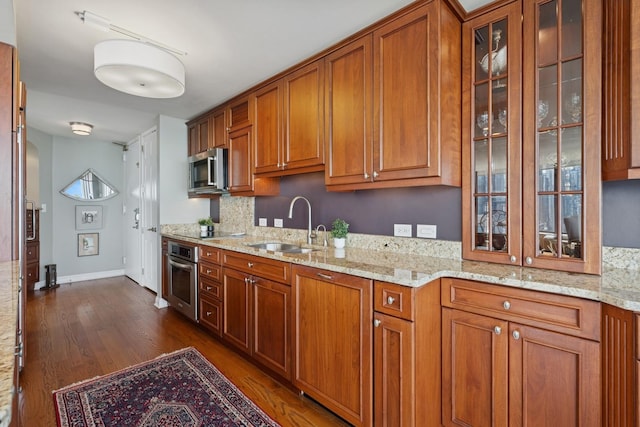 kitchen featuring brown cabinets, a sink, light stone counters, dark wood-style floors, and stainless steel appliances