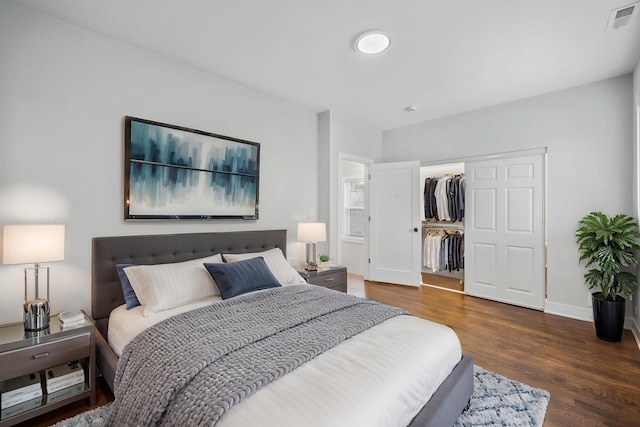 bedroom featuring a walk in closet, baseboards, wood finished floors, visible vents, and a closet