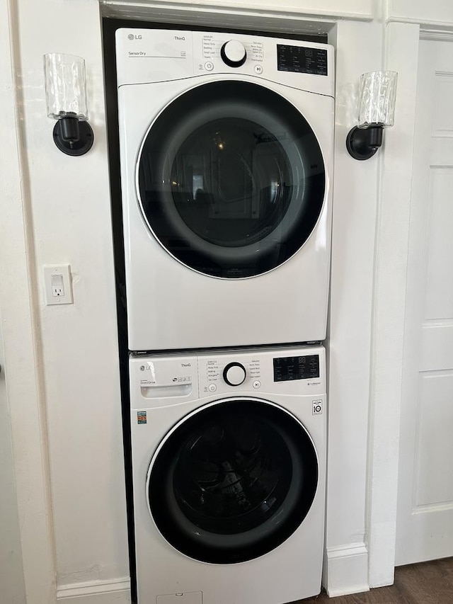 washroom featuring laundry area, stacked washer and clothes dryer, baseboards, and wood finished floors