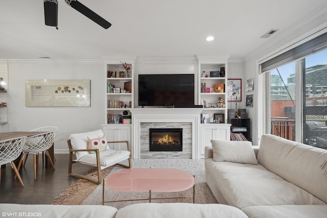 living room with crown molding, visible vents, wood finished floors, ceiling fan, and a tile fireplace