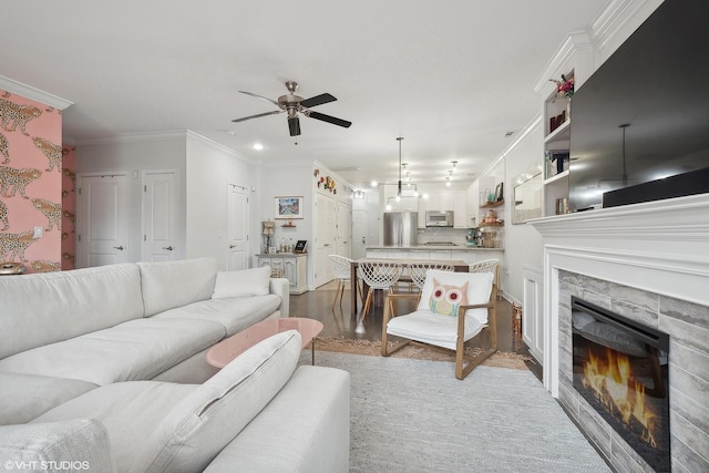 living room featuring a ceiling fan, a fireplace, ornamental molding, recessed lighting, and light wood-style flooring