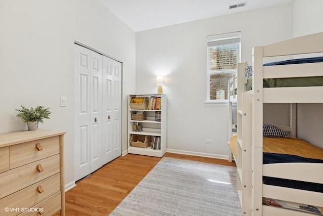 bedroom with light wood-style floors, baseboards, visible vents, and a closet