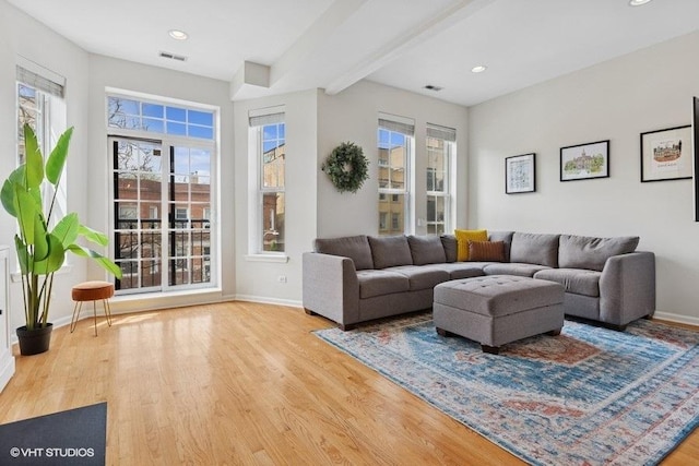 living area with beamed ceiling, visible vents, baseboards, and wood finished floors