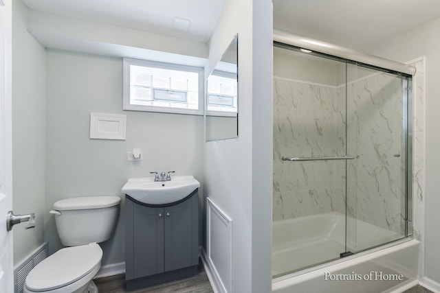 bathroom with visible vents, wood finished floors, vanity, combined bath / shower with glass door, and toilet