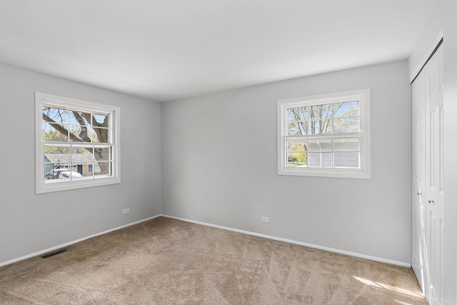 unfurnished bedroom with carpet flooring, visible vents, multiple windows, and a closet
