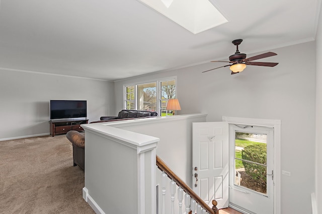 living area featuring ceiling fan, a skylight, baseboards, ornamental molding, and light carpet