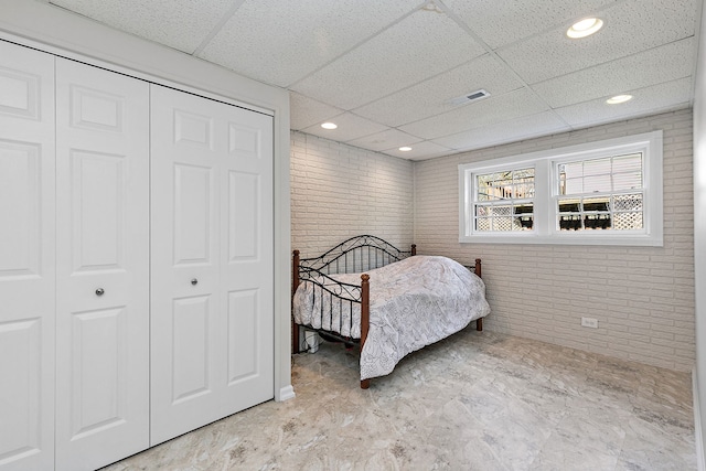 bedroom with brick wall, visible vents, a paneled ceiling, and a closet