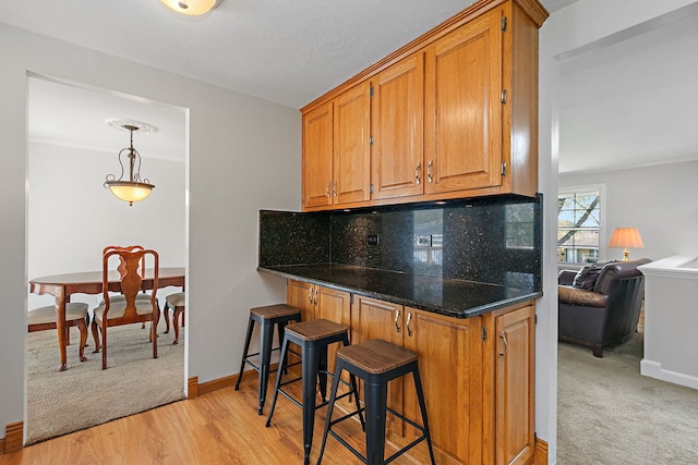 kitchen with brown cabinetry, decorative backsplash, dark countertops, baseboards, and a kitchen breakfast bar
