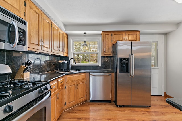 kitchen with decorative backsplash, brown cabinets, a sink, light wood-style flooring, and stainless steel appliances