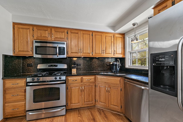 kitchen featuring brown cabinetry, decorative backsplash, a sink, light wood-style flooring, and stainless steel appliances