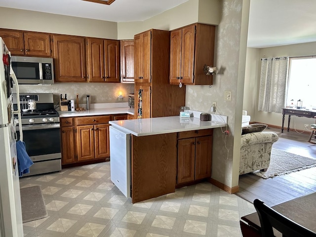 kitchen with brown cabinetry, a peninsula, light floors, light countertops, and appliances with stainless steel finishes
