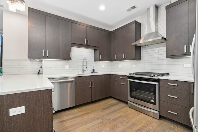 kitchen with visible vents, wall chimney exhaust hood, a sink, light wood-style flooring, and appliances with stainless steel finishes